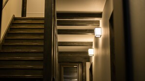 A staircase with wooden steps and a handrail, leading to a door with a light fixture above it. - JINYA Fujikawaguchiko (Fujikawaguchiko)