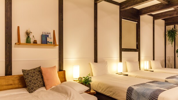 A hotel room with two beds, wooden beams, a shelf with books and a vase, and a mirror on the wall. - JINYA Fujikawaguchiko (Fujikawaguchiko)