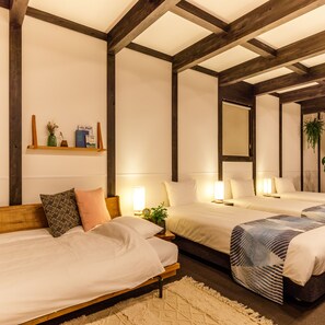 Habitación de hotel con dos camas, vigas de madera, una estantería con libros y un jarrón, y un espejo en la pared.