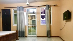 A room with a bed, a TV mounted on the wall, and a sliding glass door leading to a balcony. - Just Home (Zanzibar Town)