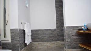 A bathroom with a shower, a toilet, a towel rack, and a soap dispenser on a shelf. - Just Home (Zanzibar Town)