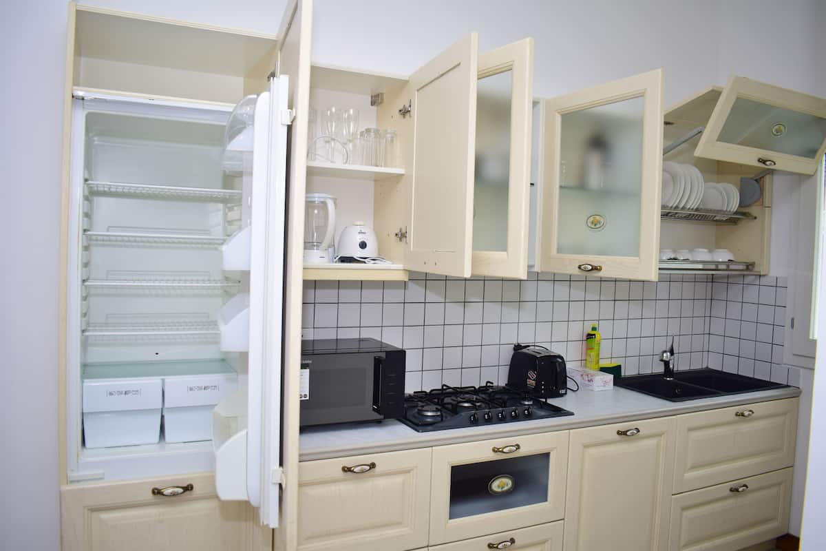 Een keuken met open kastjes, een magnetron, een kookplaat en een spoelbak.