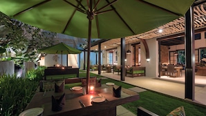 An outdoor dining area with a green umbrella, wooden tables, and chairs. - Kemangi Bed & Breakfast (Kuta)