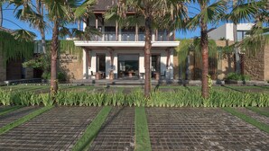 A two-story building with a balcony, surrounded by palm trees and a well-maintained garden with a paved walkway. - Kemangi Bed & Breakfast (Kuta)