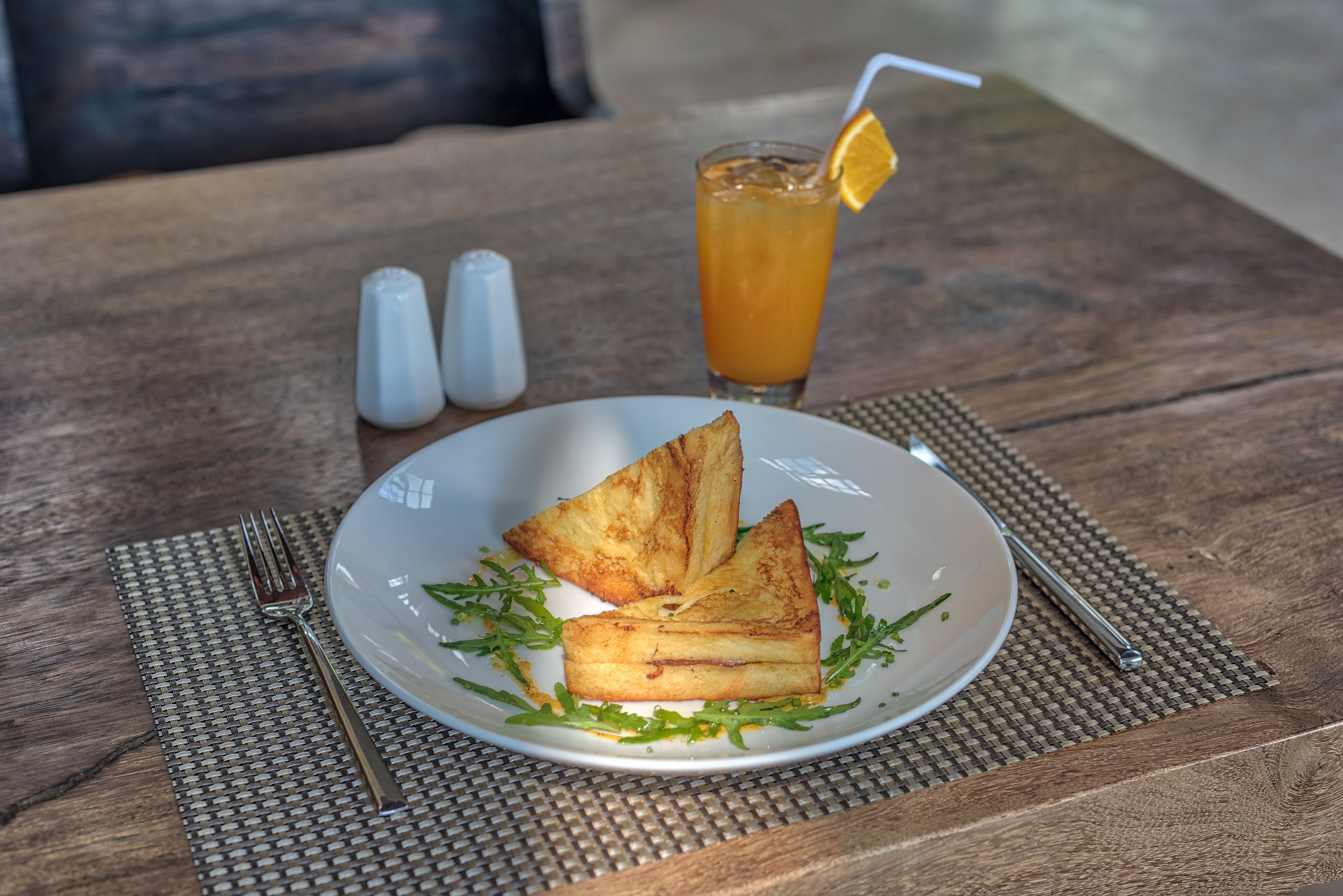 Une assiette de sandwichs grillés sur une table en bois, accompagnée d’un verre de thé glacé et d’une paille.