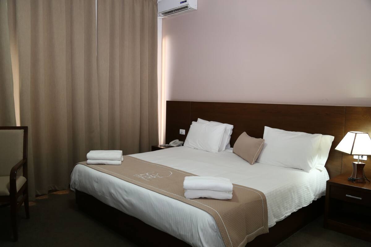 A hotel room with a large bed, a wooden headboard, a nightstand with a lamp, and a chair.