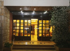 Entrada de hotel con fachada de madera, puertas de cristal y una escalera que sube.