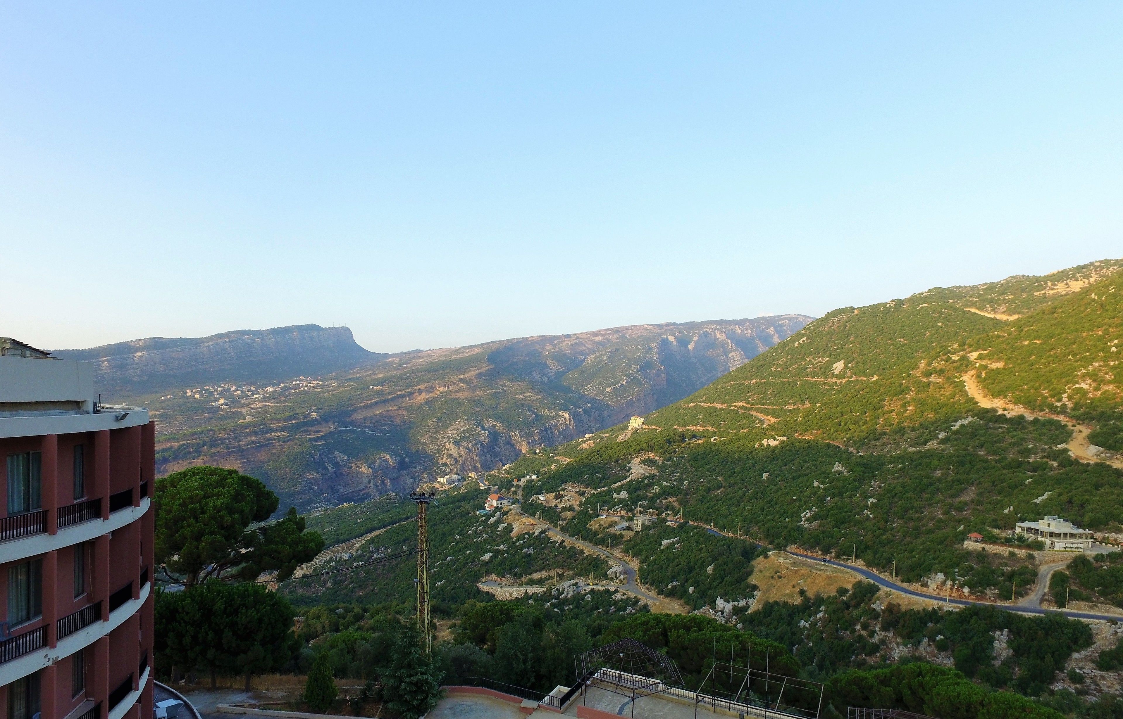 A mountainous landscape with a road winding through it. There is a building with multiple floors in the foreground.