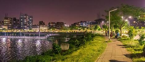 Vista nocturna de un paseo fluvial con un puente, edificios al fondo y farolas.