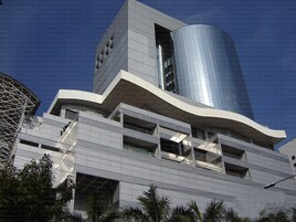 Un edificio moderno con fachada curva, varios balcones y una torre cilíndrica de vidrio.