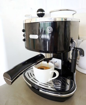Una máquina de espresso negra y plateada con una taza blanca debajo, sobre una encimera.