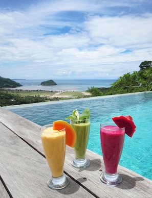 Una terraza de madera con tres batidos de fruta y vista a una playa y al océano.