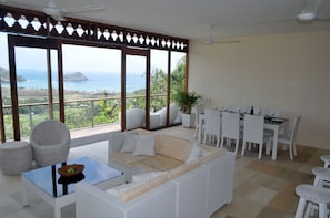 Enjoy a panoramic ocean view from this room's large window, featuring a comfortable sofa set and dining area.