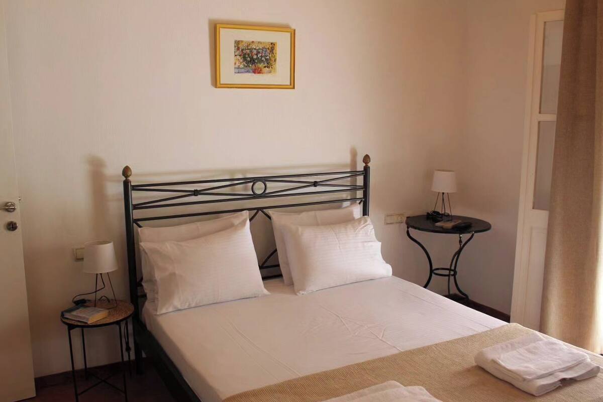 A neatly made bed with white linens, two bedside tables with lamps, and a framed picture on the wall.