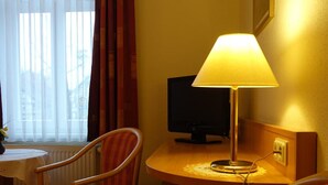 A hotel room with a wooden desk, a lamp, a television, and two striped chairs. - Pension Am Nicolaiplatz (Wernigerode)