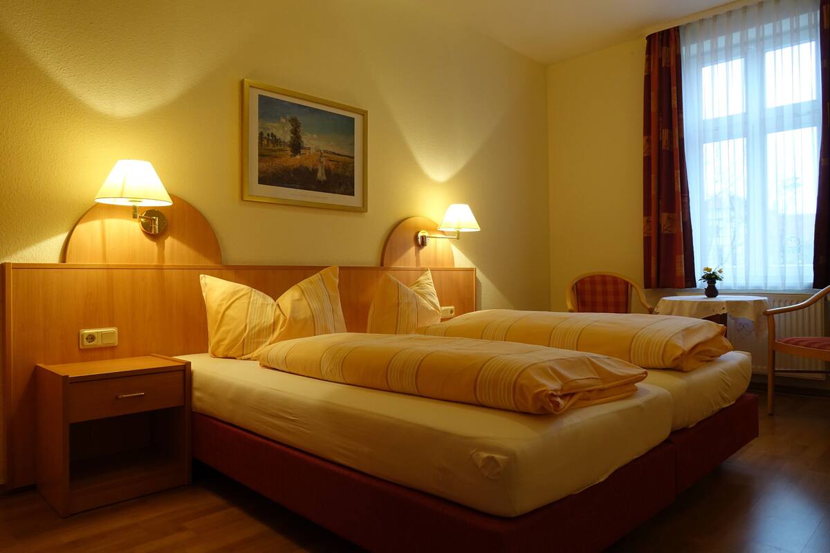 A hotel room with two beds, nightstands, a chair, a table, and a painting on the wall.