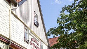 An outdoor seating area with tables and chairs, a building with a sign reading "Restaurant am Hofbräuhaus," and a red umbrella with the text "Halleröder." - Pension Am Nicolaiplatz (Wernigerode)