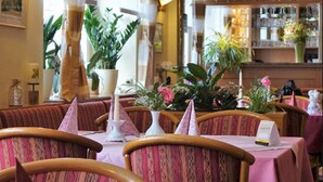 A restaurant interior with striped curtains, wooden chairs, and tables set with pink tablecloths. - Pension Am Nicolaiplatz (Wernigerode)