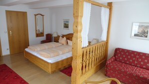 A bedroom with a wooden four-poster bed, a red sofa, and a wooden-framed window with white curtains. - Pension Am Nicolaiplatz (Wernigerode)