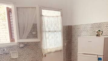 A compact kitchen with a sink, a stove, a refrigerator, and patterned walls.