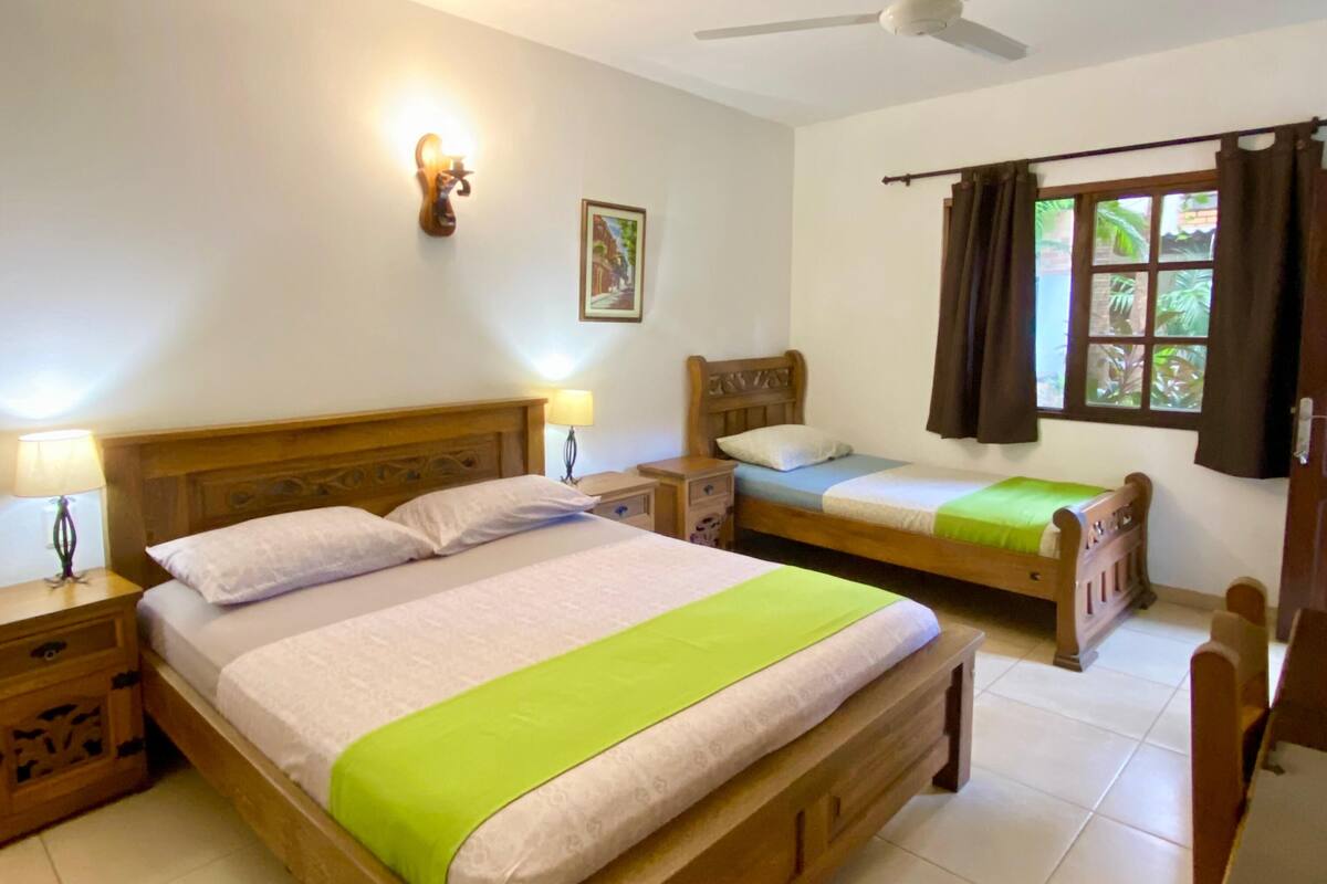 A bedroom with two wooden beds, a ceiling fan, and a window with curtains.