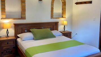Quarto com cama de madeira, duas mesas de cabeceira com luminárias e dois espelhos em arco de tijolo na parede.
