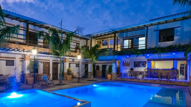 Un área de piscina con una piscina azul cristalina, sillones de descanso y una zona de bar con asientos.