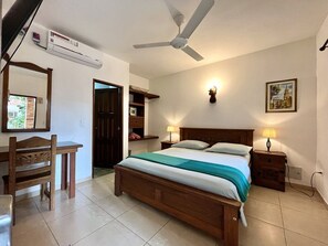 A bedroom with a bed, bedside tables, a desk, a chair, a ceiling fan, and an air conditioning unit. - Camali Hotel (Santa Marta)