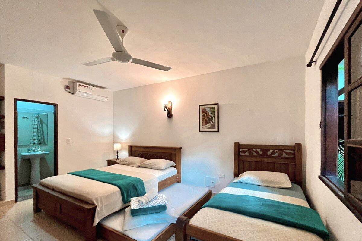 A room with two wooden beds, a ceiling fan, a wall-mounted light, and a window with blinds.