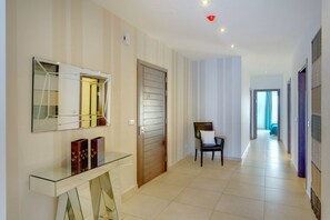 Um corredor moderno com uma mesa de consola de vidro, um espelho na parede e uma porta de madeira.