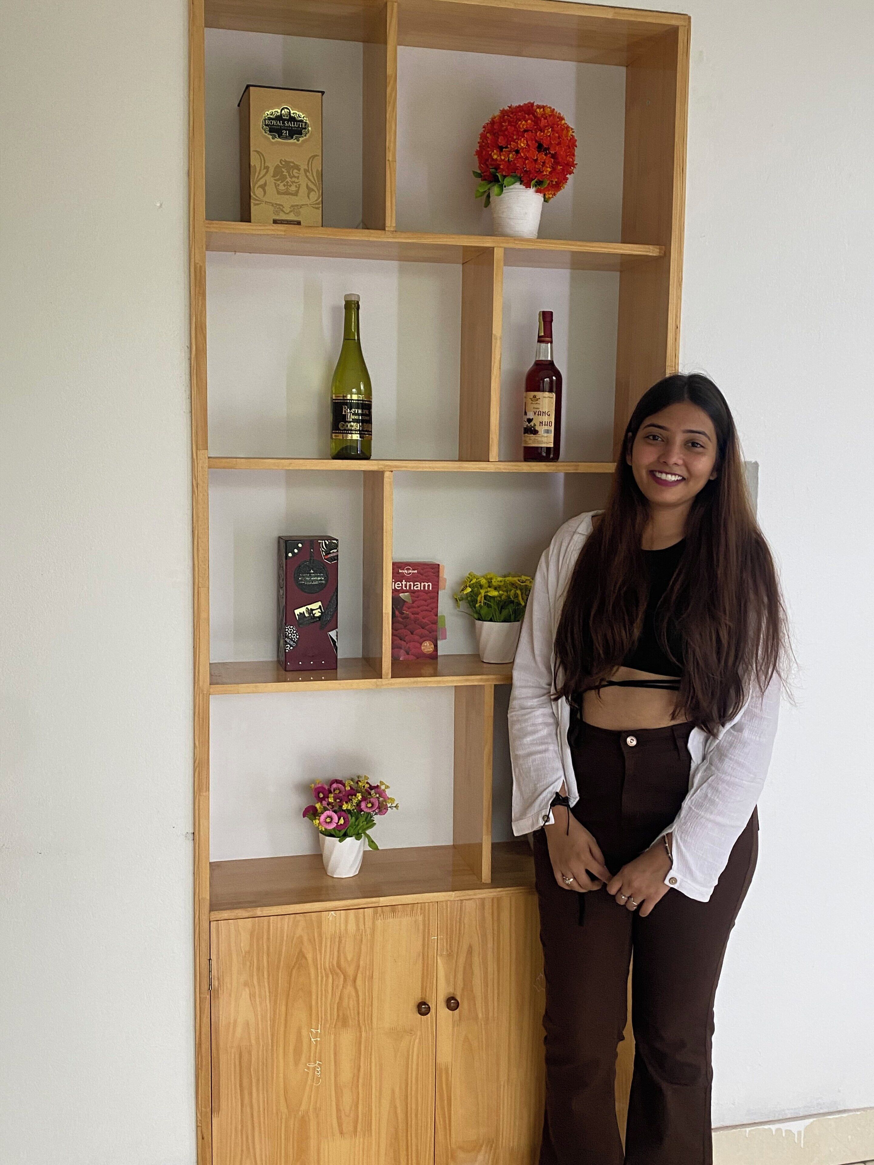 A wooden shelf with various items including a bottle, a box, and a vase with flowers.