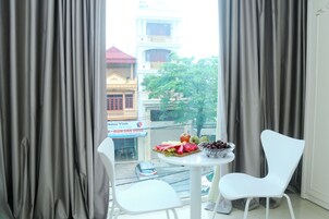 Quarto com vista para a rua, uma mesa com frutas e duas cadeiras brancas.