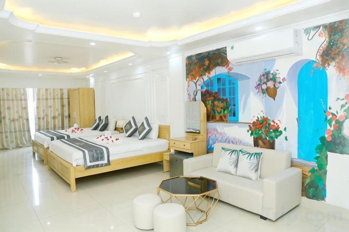 A modern bedroom with a large bed, a sofa, a coffee table, and a painting of a blue sky.