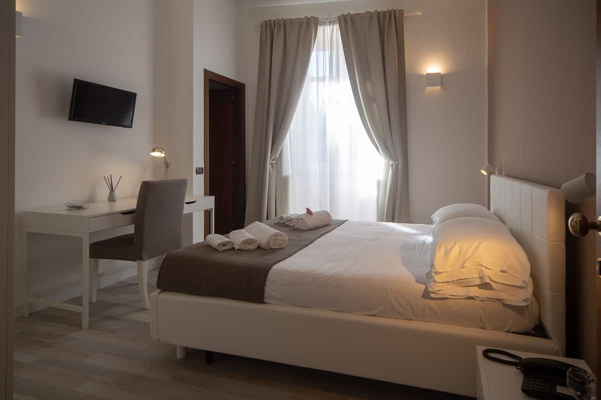 Une chambre d’hôtel équipée d’un lit, d’un bureau, d’une chaise, d’une télévision et d’un téléphone sur la table de chevet.