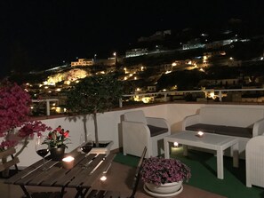 En terrass med möbler i rotting, ett bord med vinglas och ett ljus.
