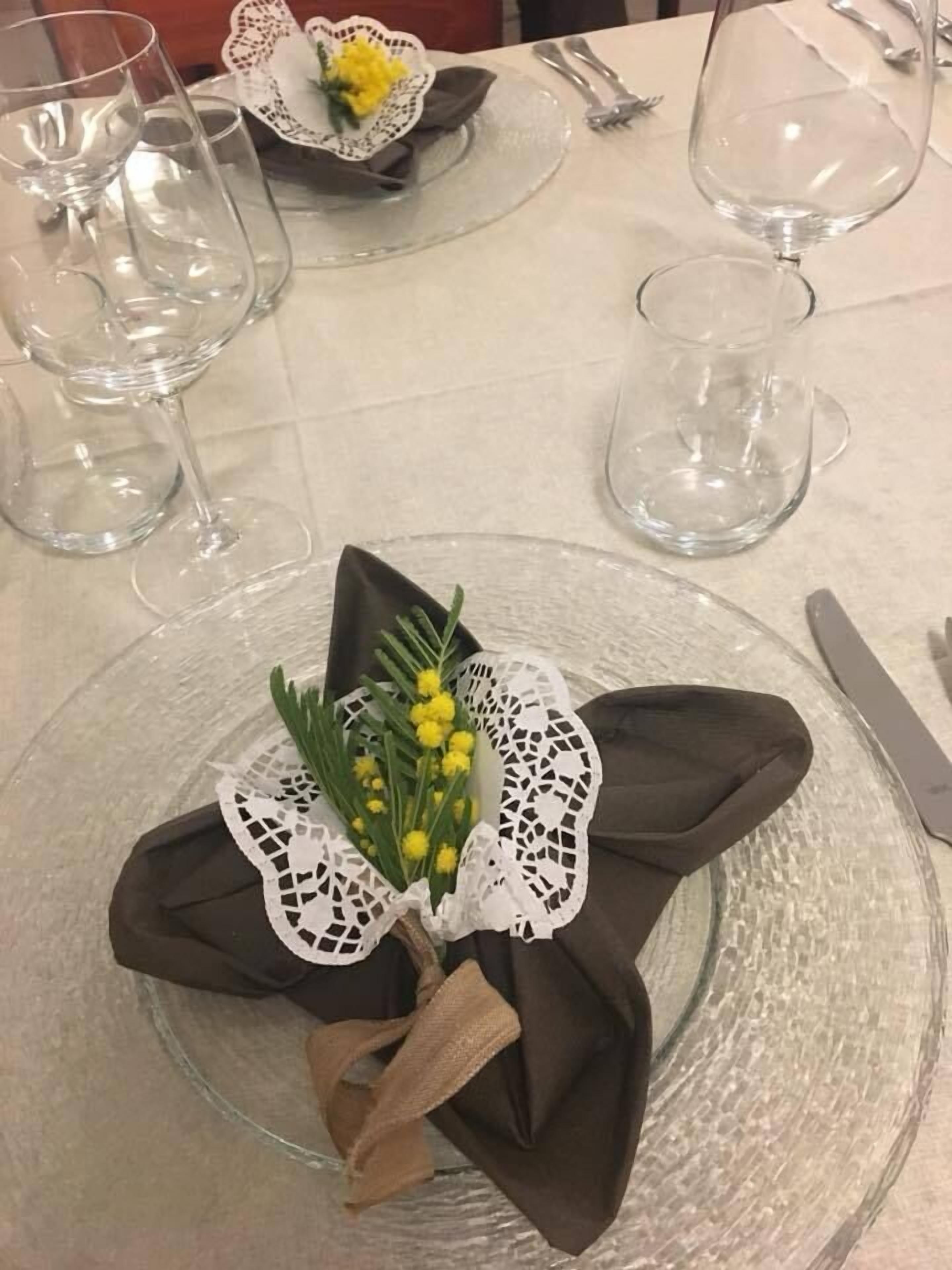 A table setting with a clear glass plate, a folded napkin, a small bouquet of yellow flowers, and a clear glass wine glass.