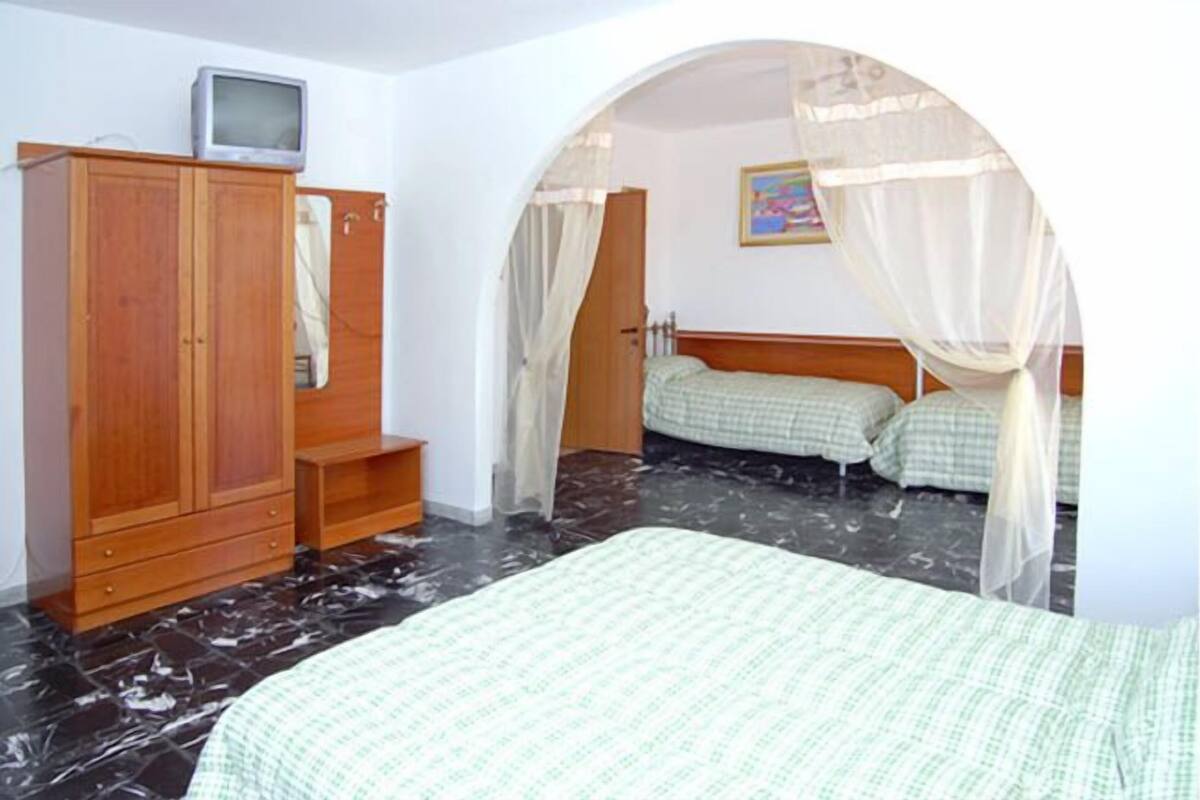 A bedroom with a bed, a wardrobe, a television on top, and a painting on the wall.