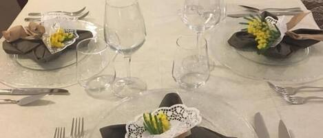 A long dining table set with clear glassware, plates, and cutlery, with napkins folded and a decorative flower arrangement.