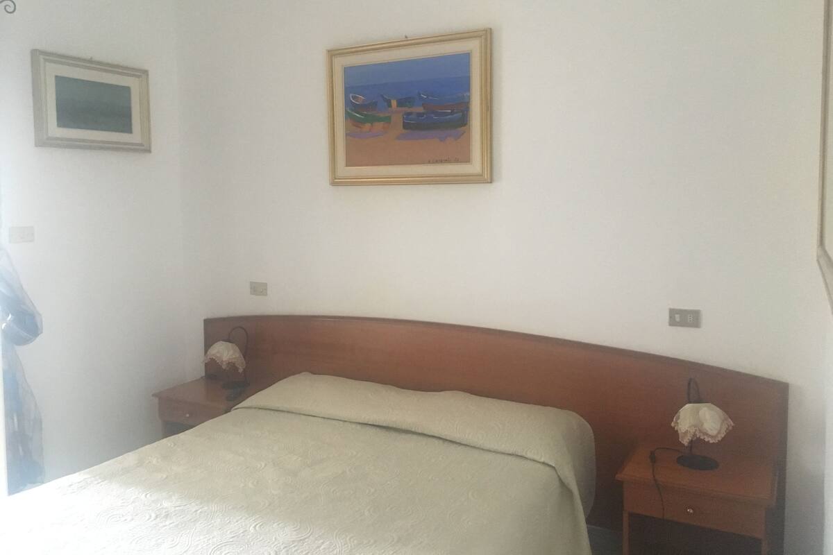 A bedroom with a bed, a nightstand, a lamp, and two framed pictures on the wall.