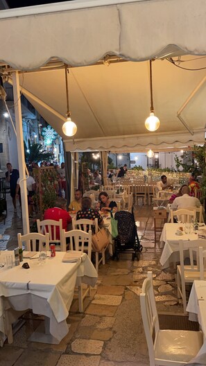 An outdoor restaurant with tables and chairs under a white canopy, stone flooring, and string lights. - Locanda Al Castello (Peschici)