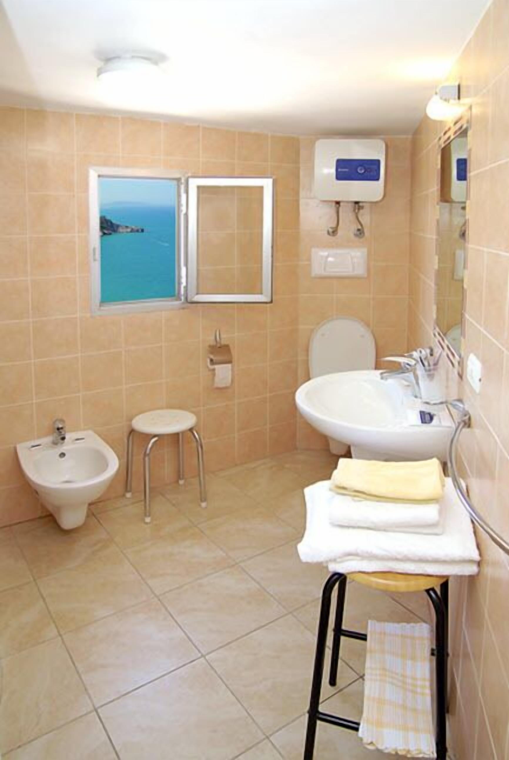 A bathroom with a bidet, a sink, a toilet, and a window with a view of the sea.