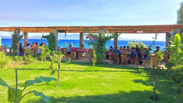 An outdoor seating area with tables and chairs under a wooden pergola, overlooking a body of water. - Sahin Motel & Restaurant (Bodrum)
