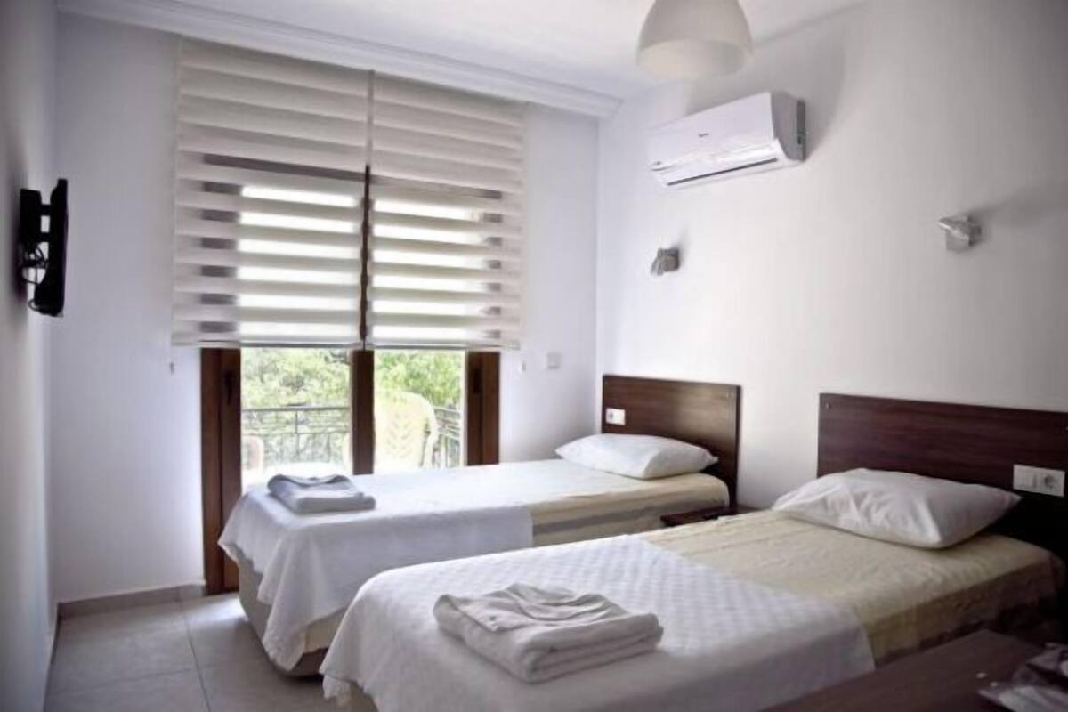 Une chambre d’hôtel avec deux lits, une fenêtre avec des stores, un appareil de climatisation et un téléviseur fixé au mur.