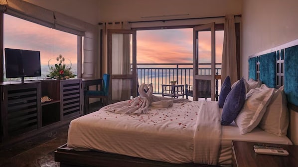 Habitación de hotel con cama, televisor, balcón con vistas y escritorio con silla.