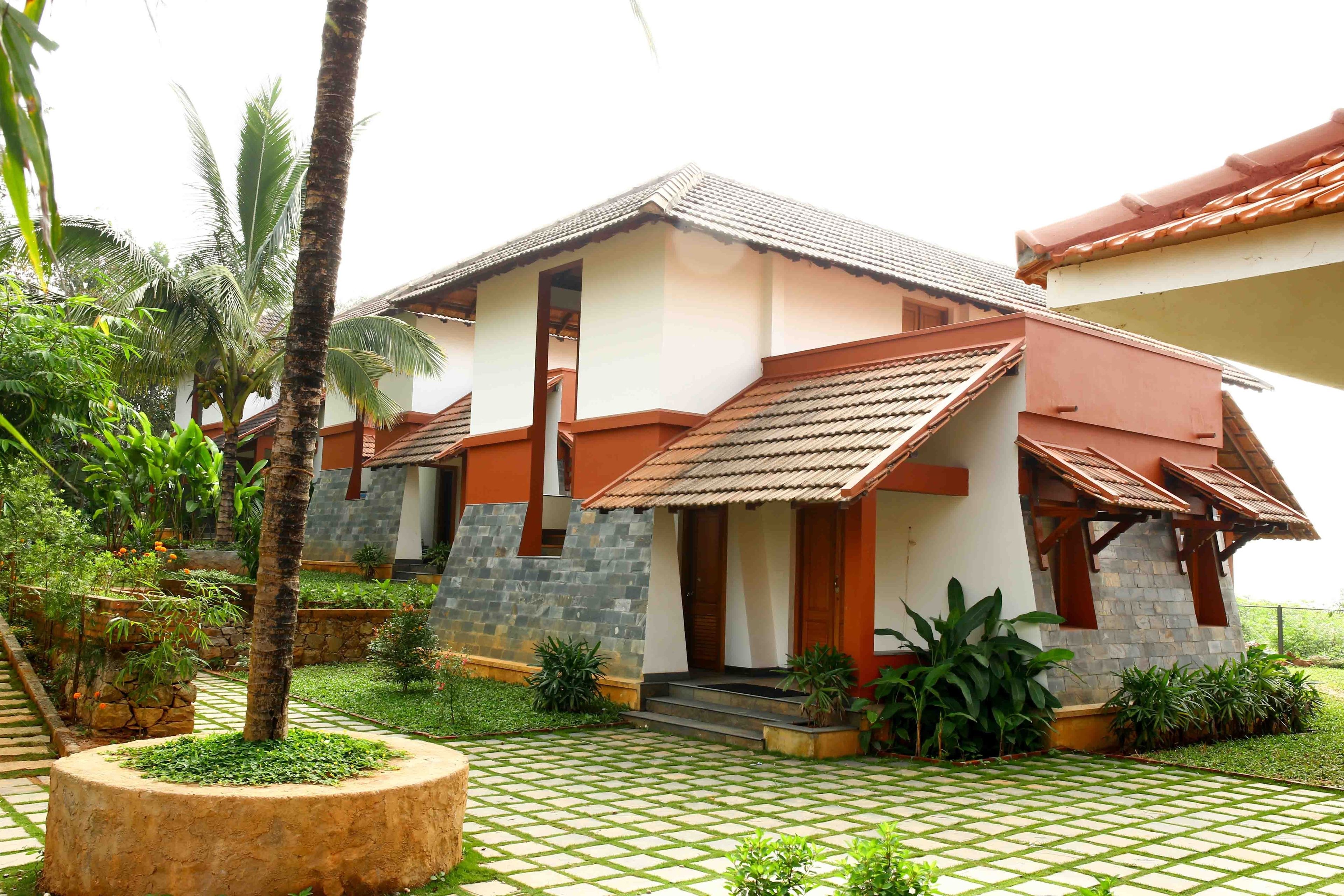 A modern house with a tiled roof, a stone facade, and a garden with palm trees and potted plants.