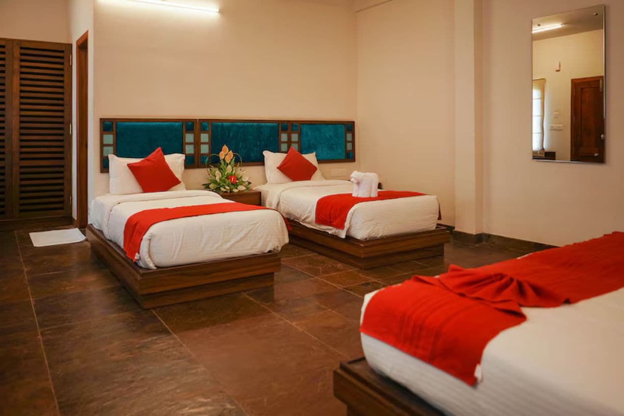 A hotel room with two beds, a wooden headboard, a mirror, and a small table with a vase.