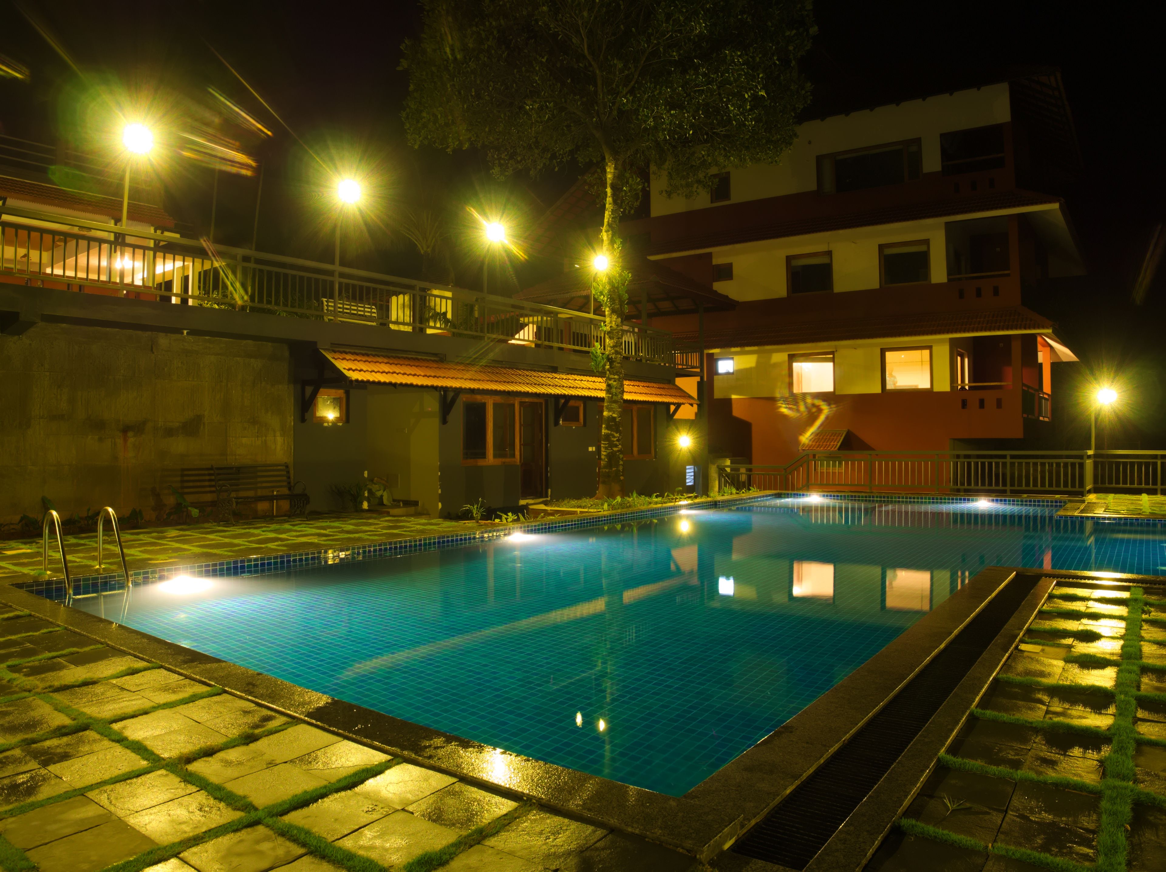 A swimming pool at night with surrounding buildings and a staircase.