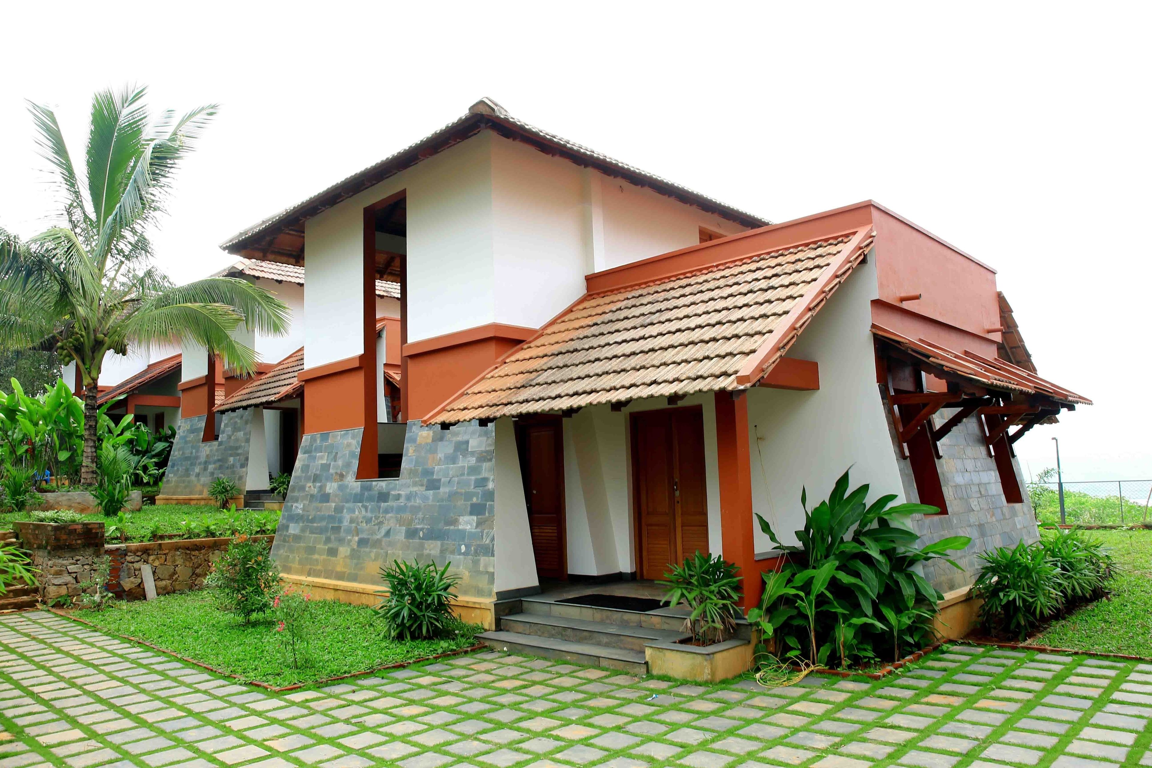 A two-story house with a tiled roof, stone walls, and a paved front yard with plants.