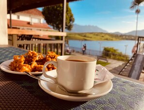 Una mesa con una taza de café y un plato de comida, con vista a un cuerpo de agua y montañas.
