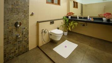A bathroom with a tiled shower wall, a toilet, a sink with a mirror above, and a potted plant on the counter.